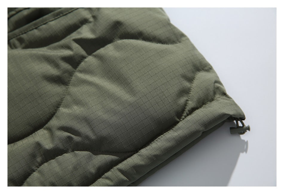 Close-up of an olive quilted jacket hem with a fine grid texture and an adjustable cord toggle.