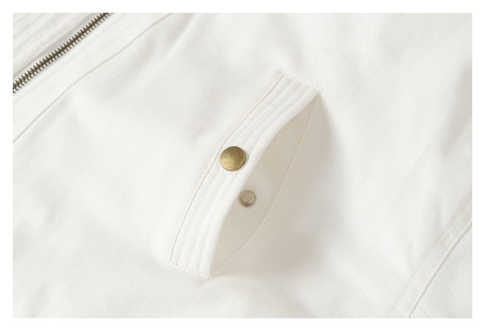 Close-up of a white jacket's angled pocket flap with two round metal snaps beside the zipper.
