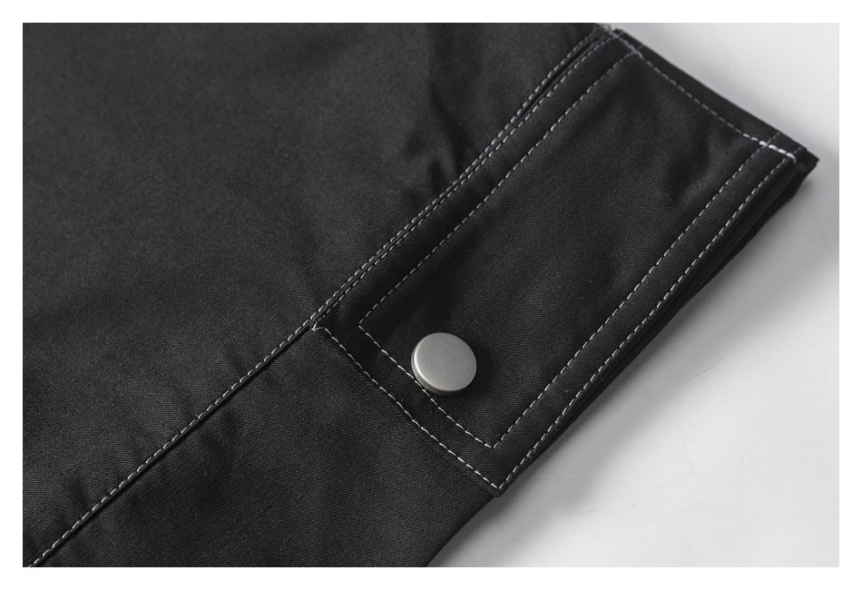 Black garment detail with a stitched rectangular tab and silver snap fastener.