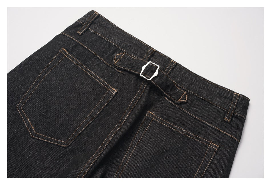 Close-up of black denim trousers' back waistband, belt loops, rear pockets and silver buckle with tan stitching.