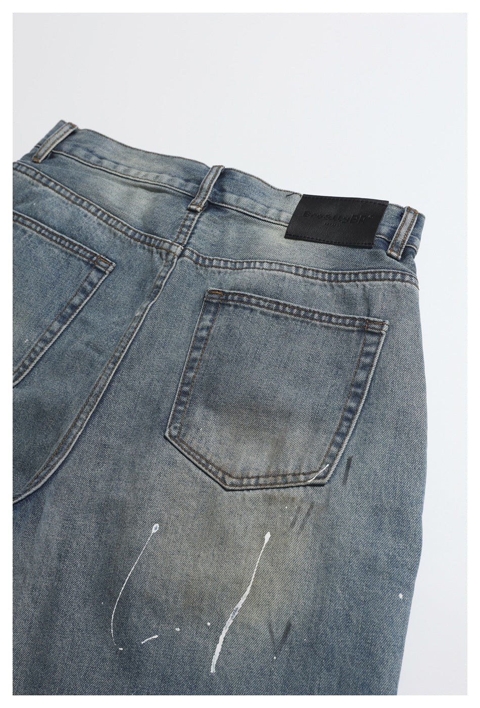 Close-up of the back waistband and pocket of blue-gray jeans, with a dark patch and white paint streaks.