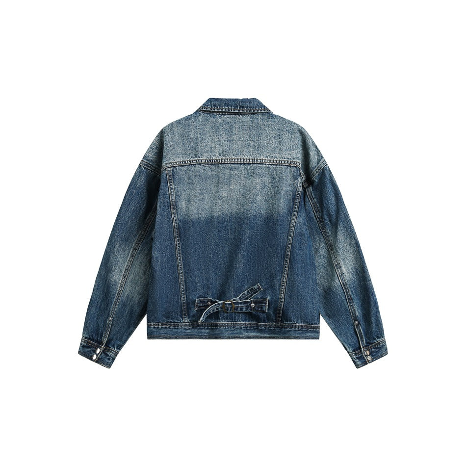 Back view of blue washed denim jacket with yoke seam, buckle strap at hem and snap cuffs