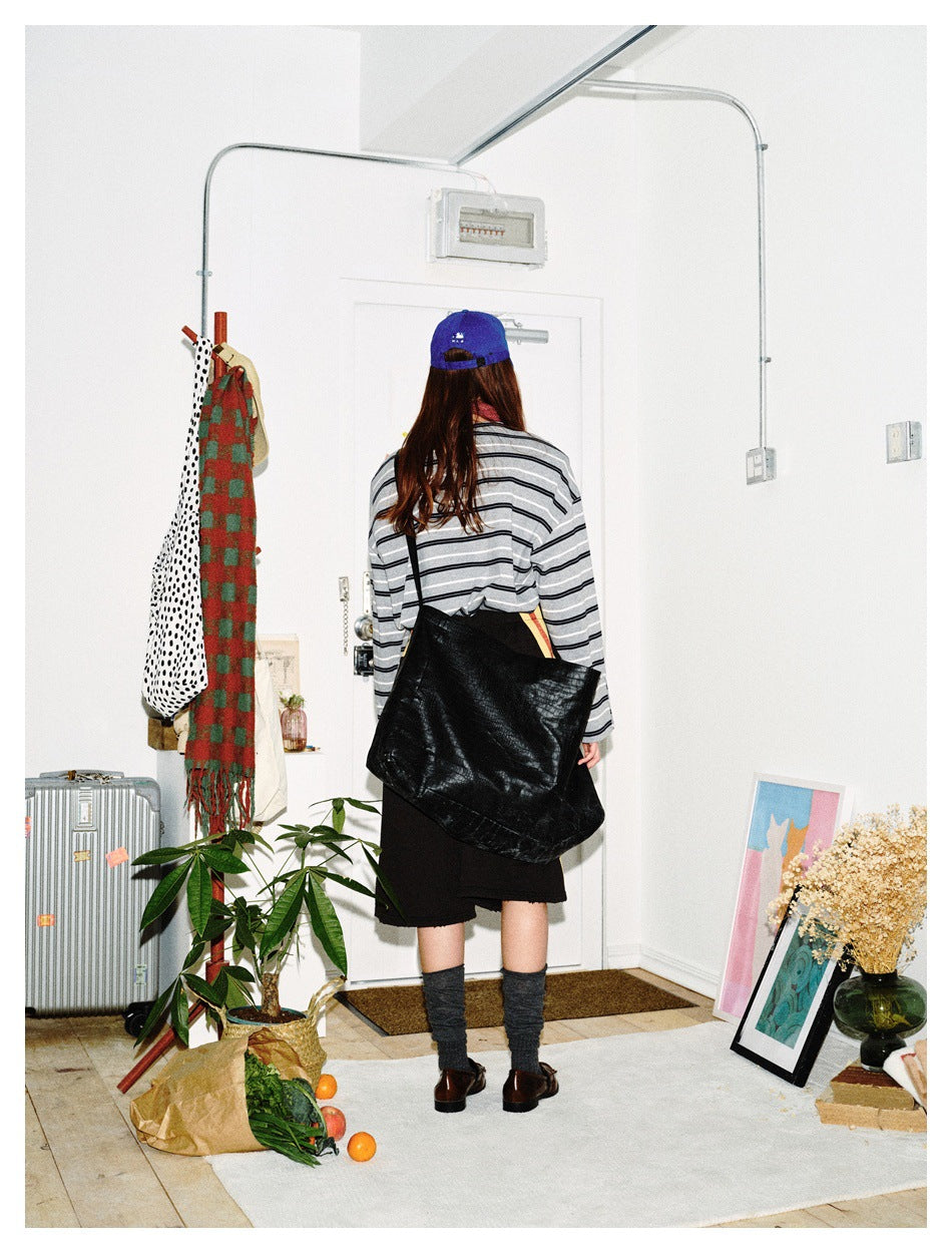 Back view of a model in a gray-and-black striped top and black shorts, with a large black shoulder bag.