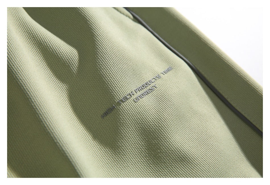 Close-up of pale sage trouser fabric with small gray lettering and a dark piping seam.