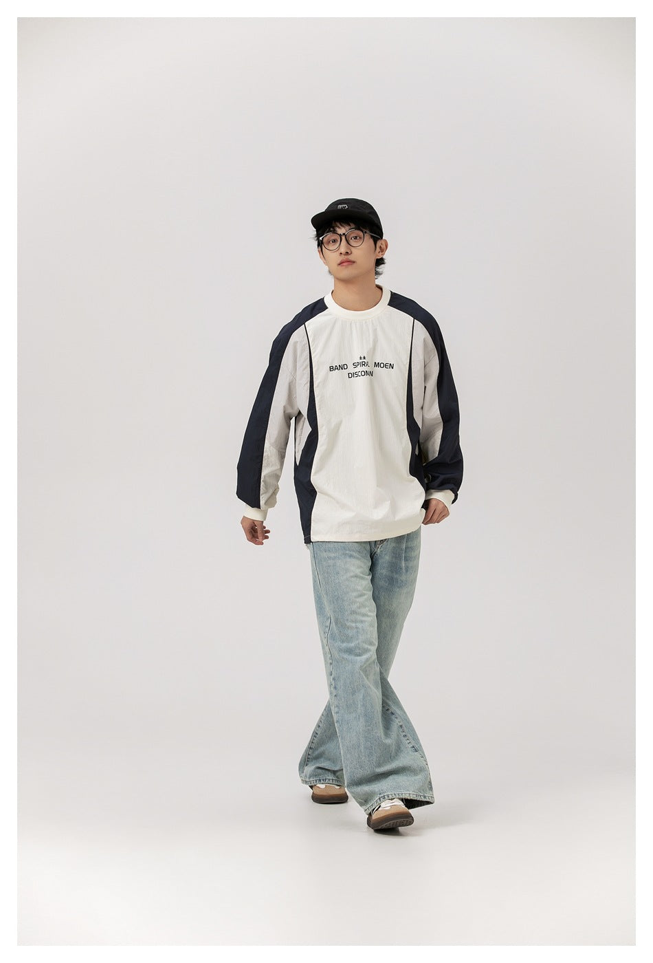 Model wearing an ivory long-sleeve top with navy panels and black chest lettering, paired with light-wash jeans.