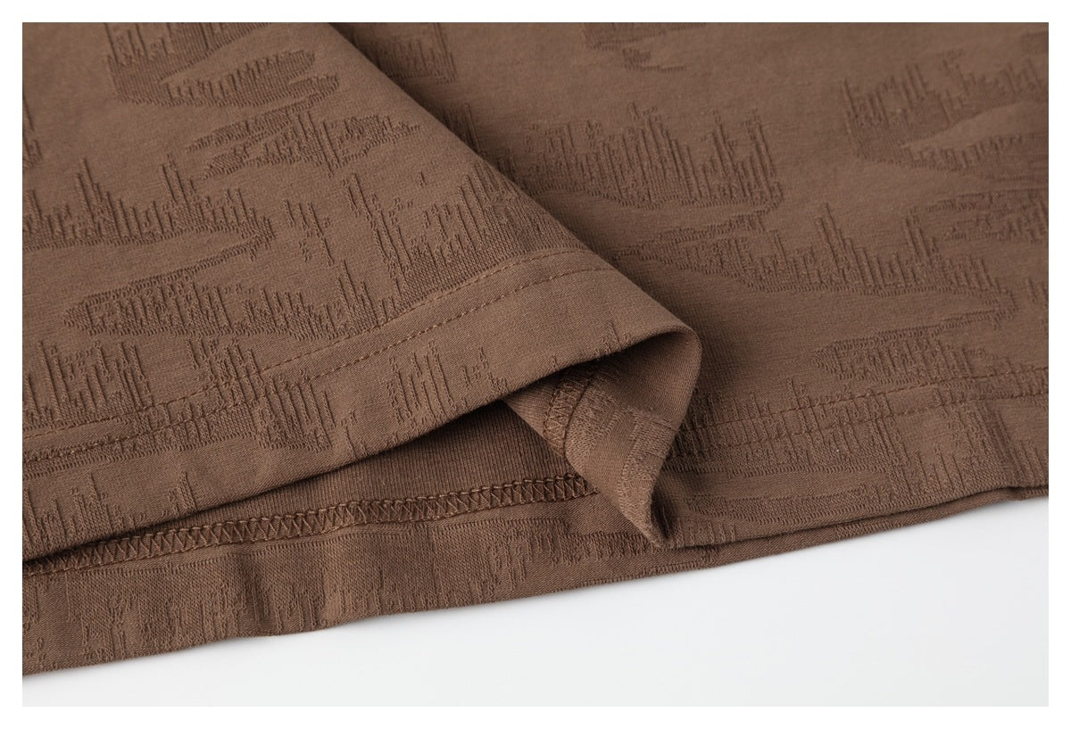 Close-up of the brown T-shirt's folded hem, stitching and raised geometric texture.