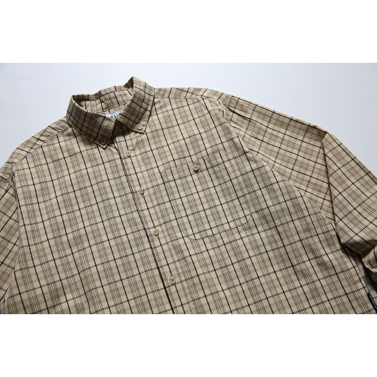 Angled close view of a beige plaid button-up shirt with a pointed collar and single chest pocket.