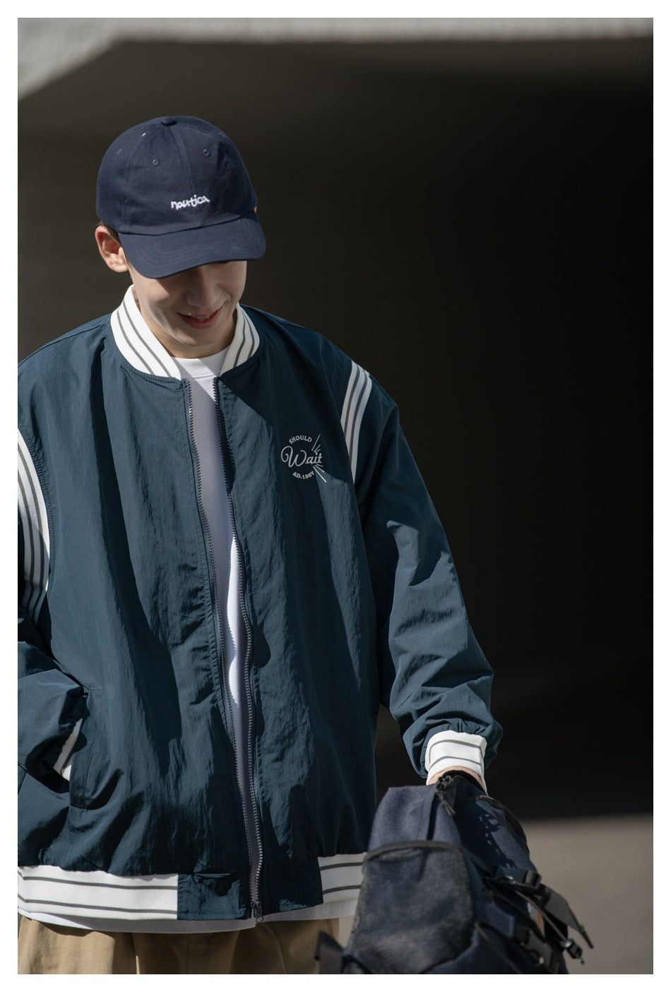 Close front view of a model wearing a dark navy zip jacket with white striped trim and a chest graphic.