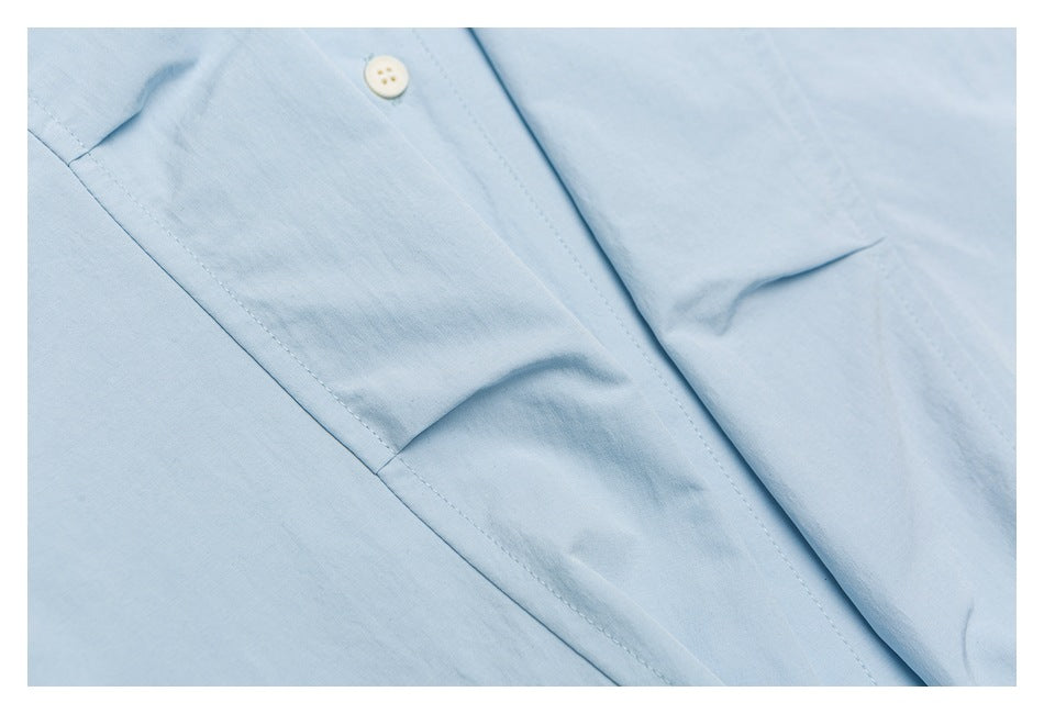 Close-up of a light blue garment showing a white button, stitched seam and overlapping fabric panels.