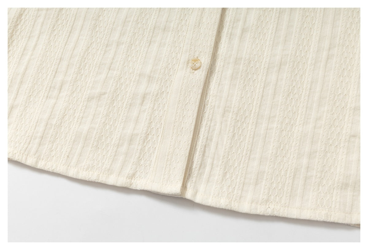 Close-up of the lower front of an ivory garment, showing a button, vertical textured bands, and the hem.