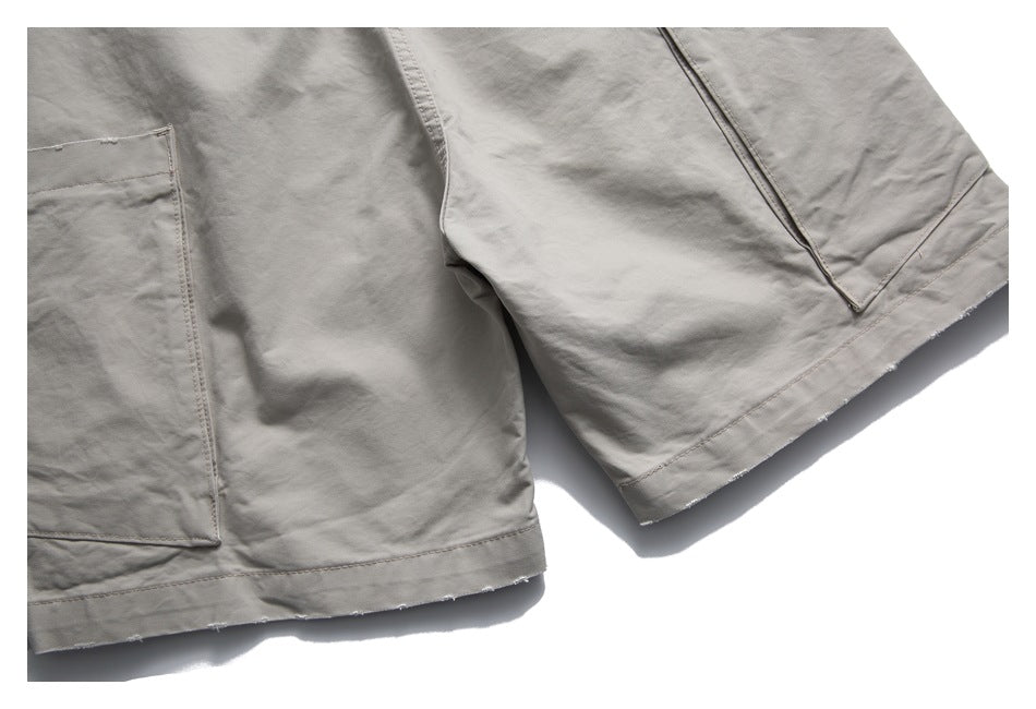 Close-up of light gray-beige shorts showing patch pockets, leg hems and visible stitching.