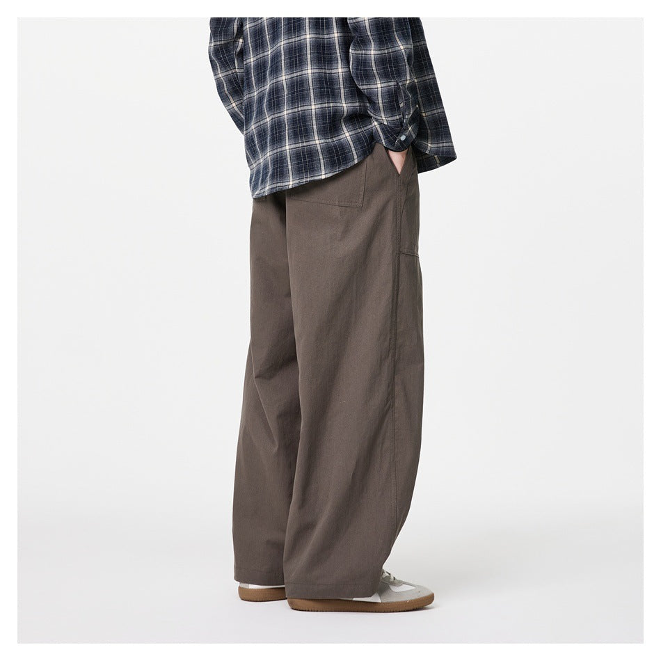 Rear three-quarter view of a model wearing dark taupe wide-leg trousers with back pockets and a navy plaid shirt.
