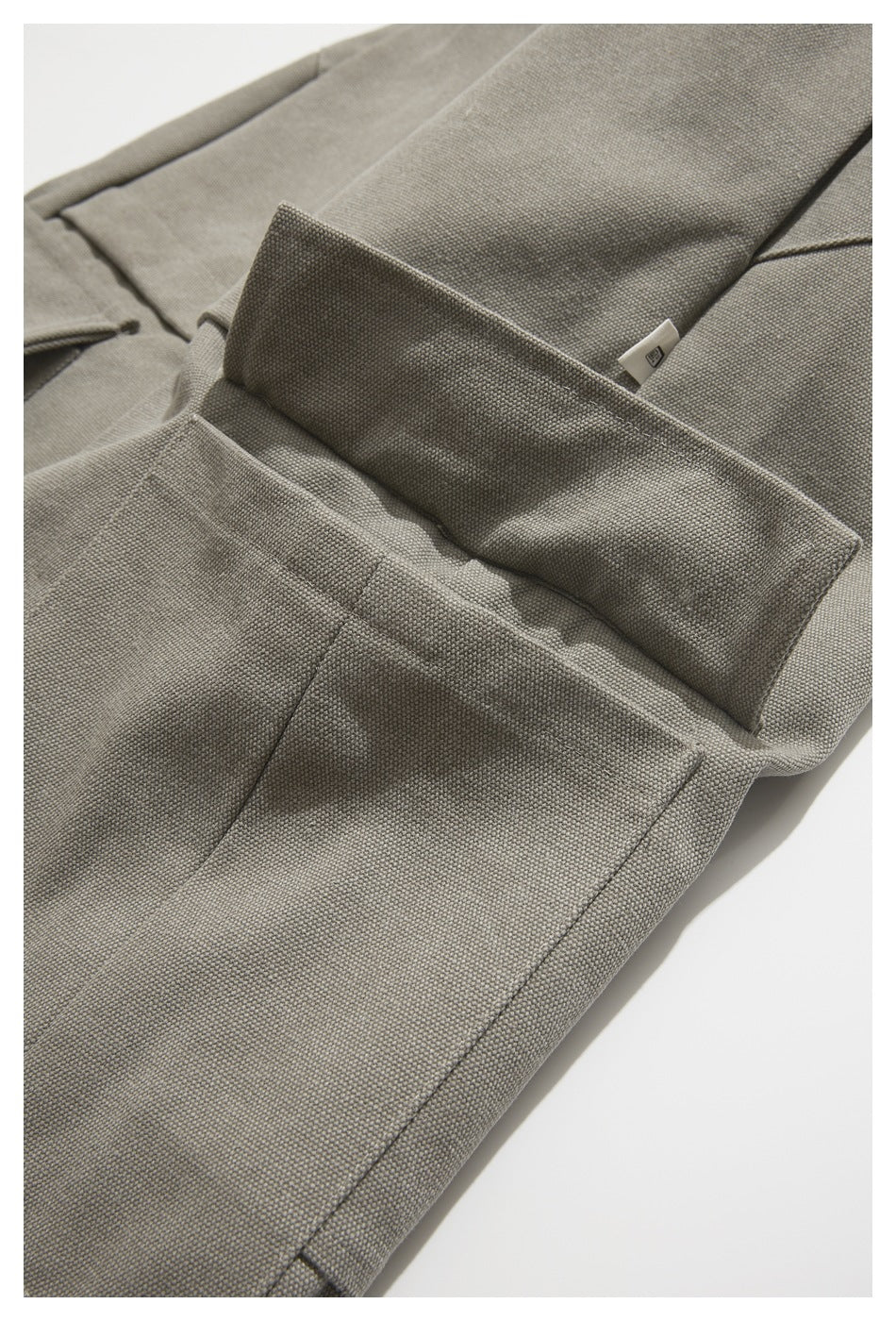 Close-up of taupe-gray trousers showing a cargo pocket with its flap lifted.