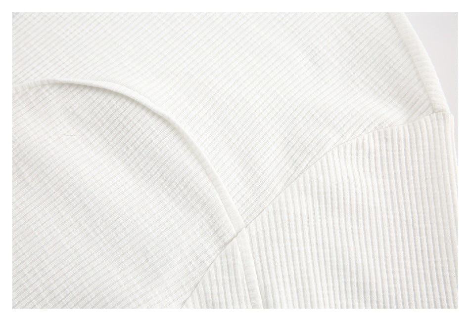 Close-up of curved seam detailing across the off-white top's fine ribbed fabric.
