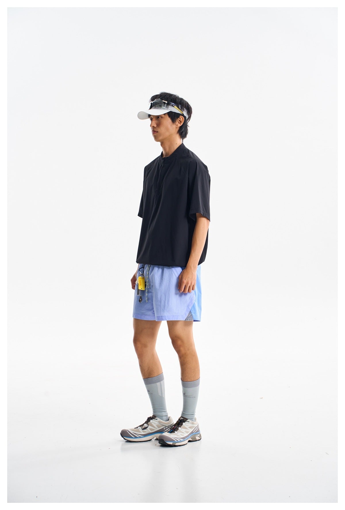 Model wearing a black short-sleeve pullover top with a short front zipper and bright blue shorts.