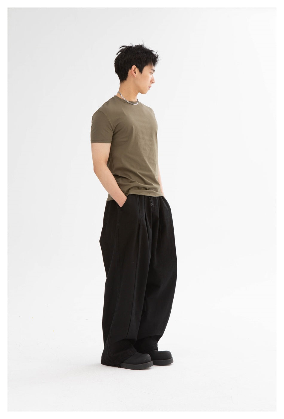 Full-length side view of a model wearing an olive-brown crew-neck T-shirt and loose black trousers.