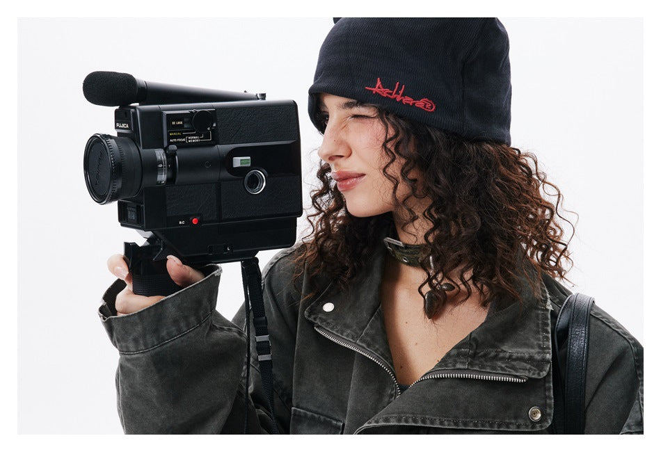Close-up of a model wearing a charcoal jacket and black beanie with red embroidery.