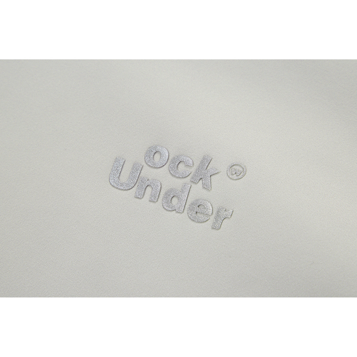 Close-up of silver embroidered lettering on light-colored jacket fabric.