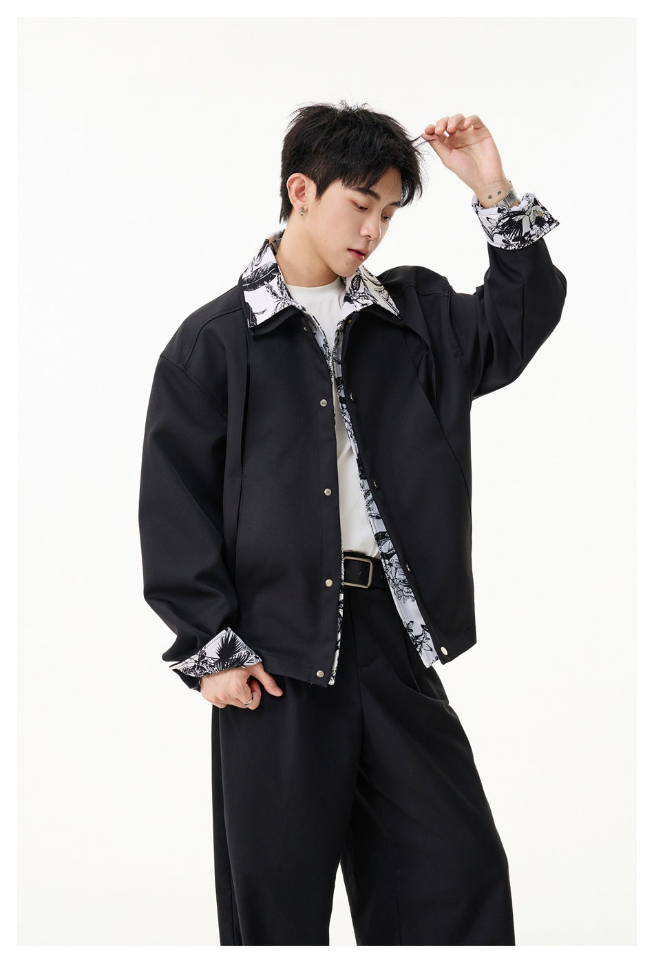 Man wearing a black snap-front jacket with black-and-white botanical print at the collar, placket and cuffs.