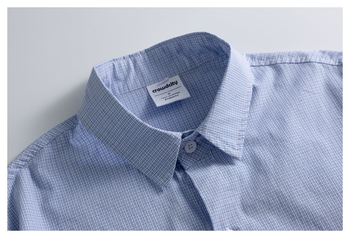 Close-up of a light blue checked shirt collar, top button, and woven brand label inside the neck.