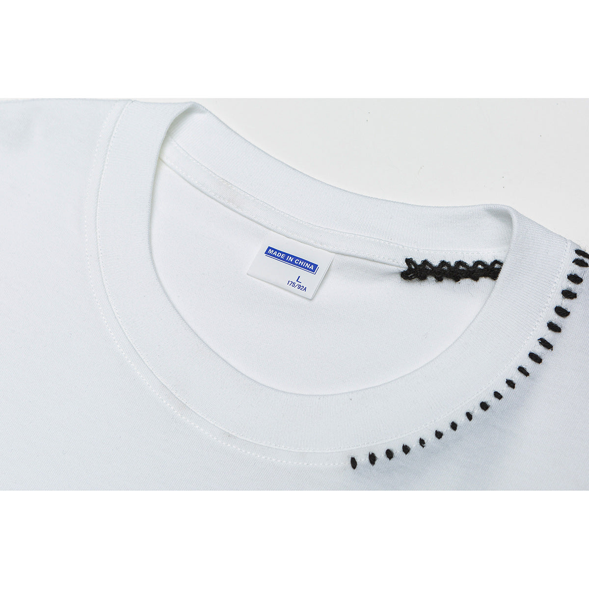 Close-up of a white T-shirt collar with black decorative stitching and a size tag.