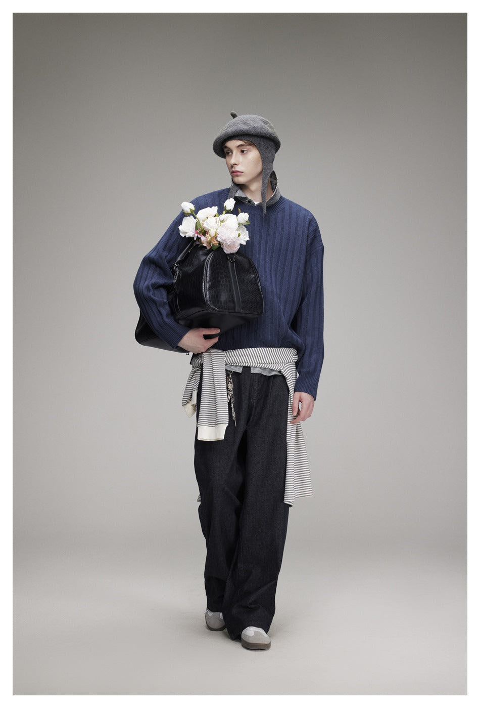 Model wearing a blue ribbed sweater and dark wide-leg jeans, holding a black bag with flowers.