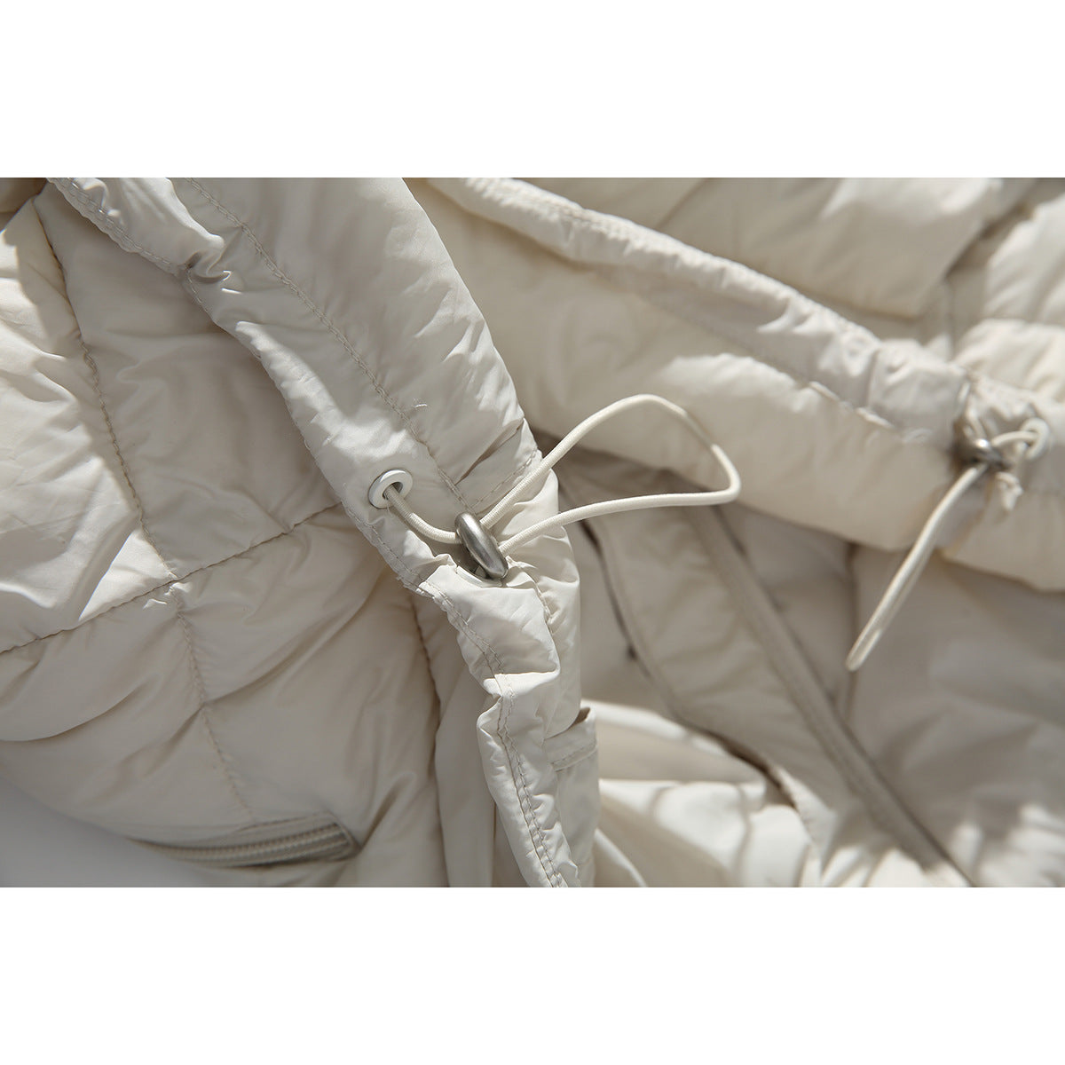 Close-up of an ivory puffer jacket's hood drawcord and toggle.