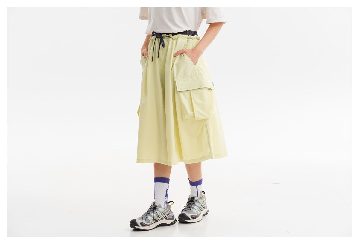 Model wearing pale yellow wide-leg cropped pants with an elastic drawstring waist and large side cargo pockets.
