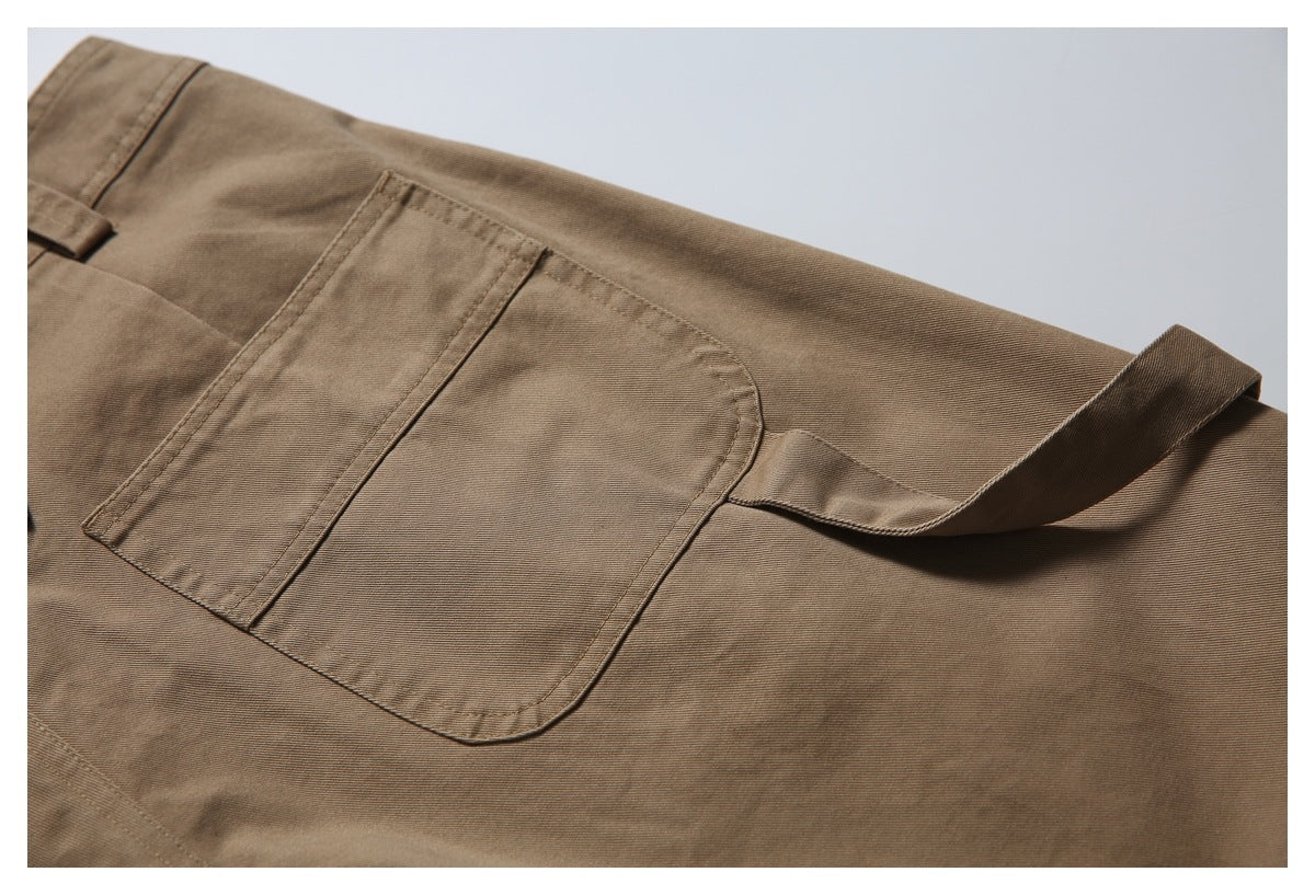 Close-up of a large stitched patch pocket and belt loop on brown utility trousers.