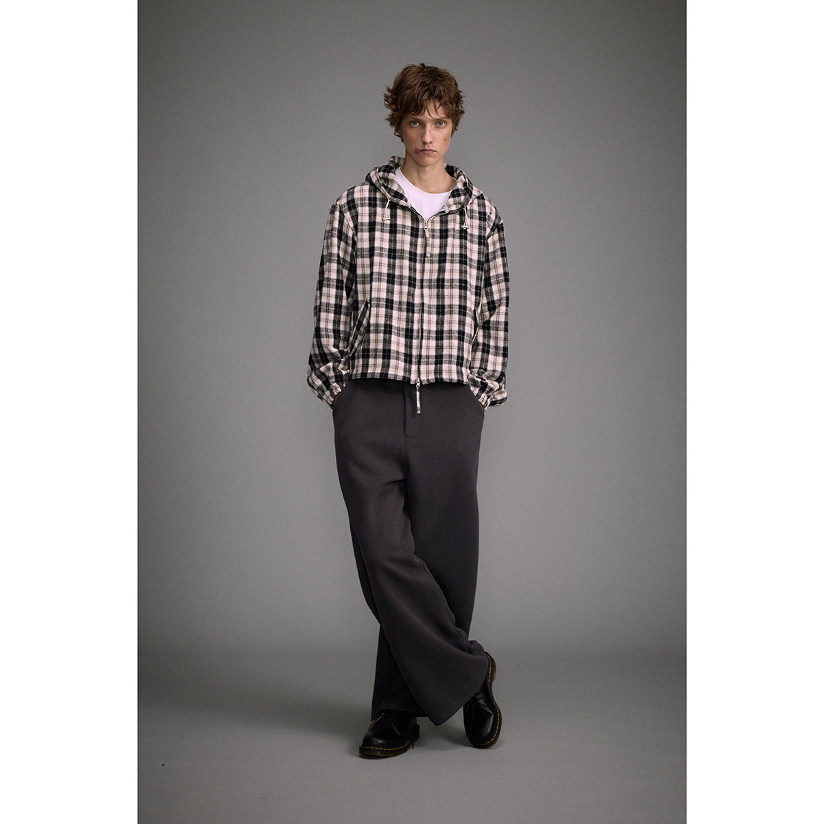 Full-length model wearing a cream and black plaid hooded jacket with dark wide-leg trousers.