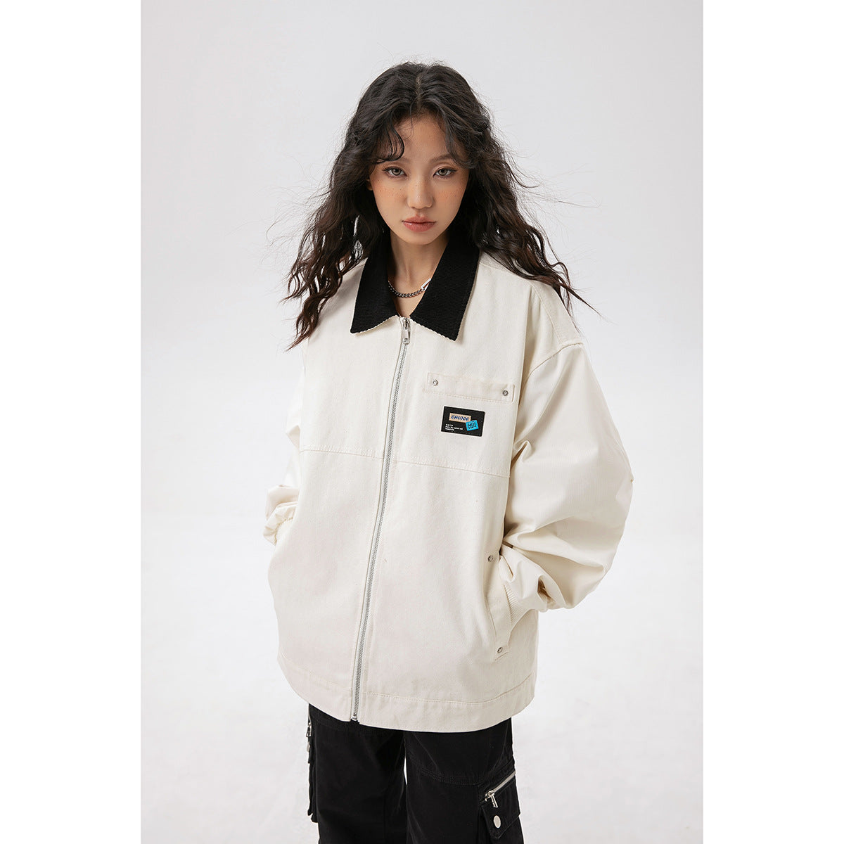 Closer front view of a model wearing an ivory jacket with a black collar, zip closure, and chest patch.