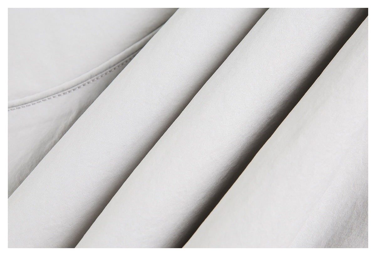 Close-up of pale gray garment fabric folded into diagonal panels, with a curved stitched seam.