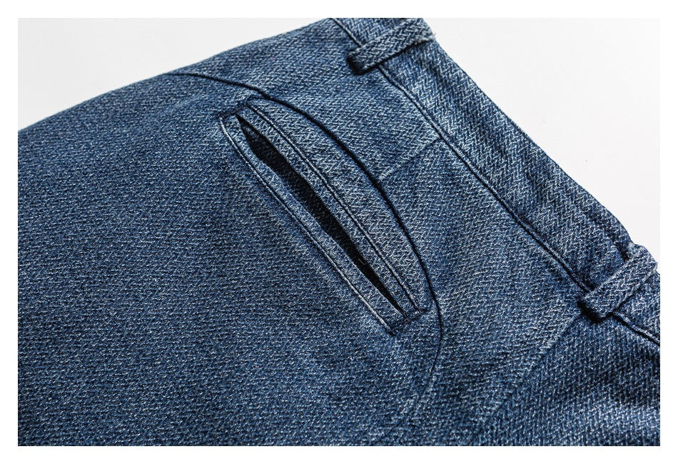 Close-up of a narrow welt pocket and belt loops on dark blue denim trousers.