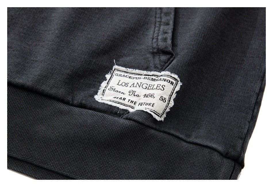 Close-up of a sewn garment label reading “Los Angeles” on charcoal fabric above a ribbed hem.