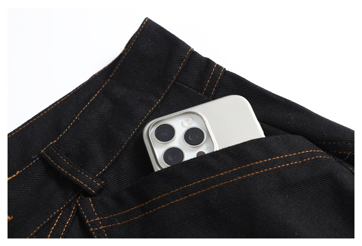 A smartphone partially tucked into a pocket on black jeans with orange stitching.