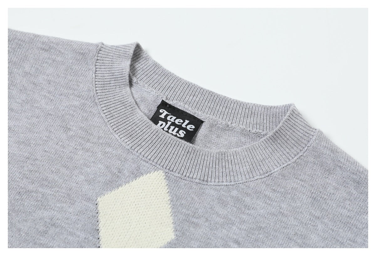 Close-up of a light gray knit sweater's ribbed crew neck and cream diamond motif, with a black sewn-in neck label.