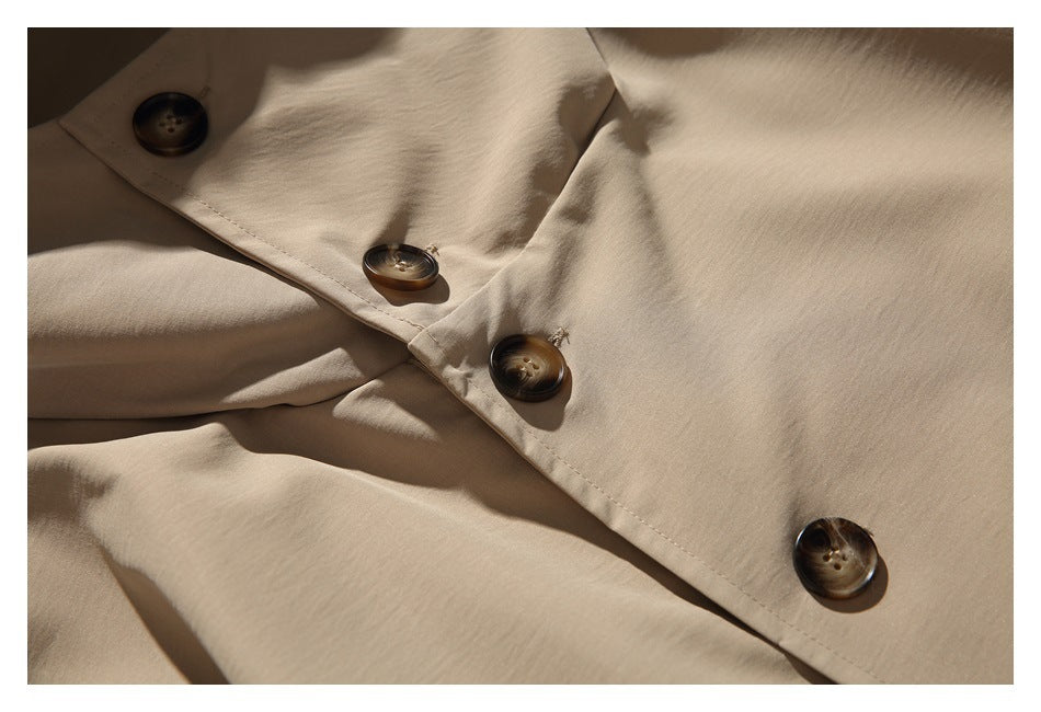 Close-up of dark brown buttons and stitching on the beige coat's front closure.