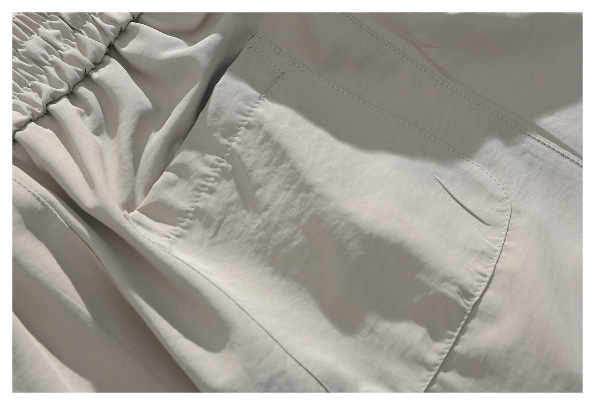 Close-up of light beige trousers showing a large stitched pocket and gathered elastic waistband.