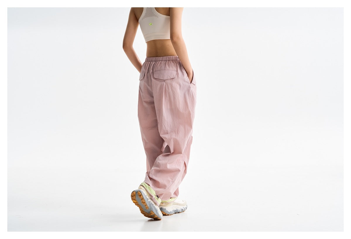 Rear view of a model wearing loose light pink pants with an elastic waist and back flap pocket.