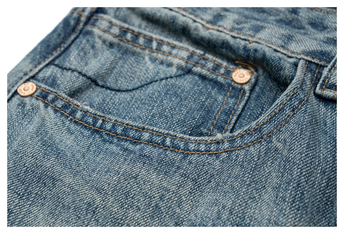 Close-up of a front pocket on faded blue jeans, with copper-colored rivets and golden stitching.