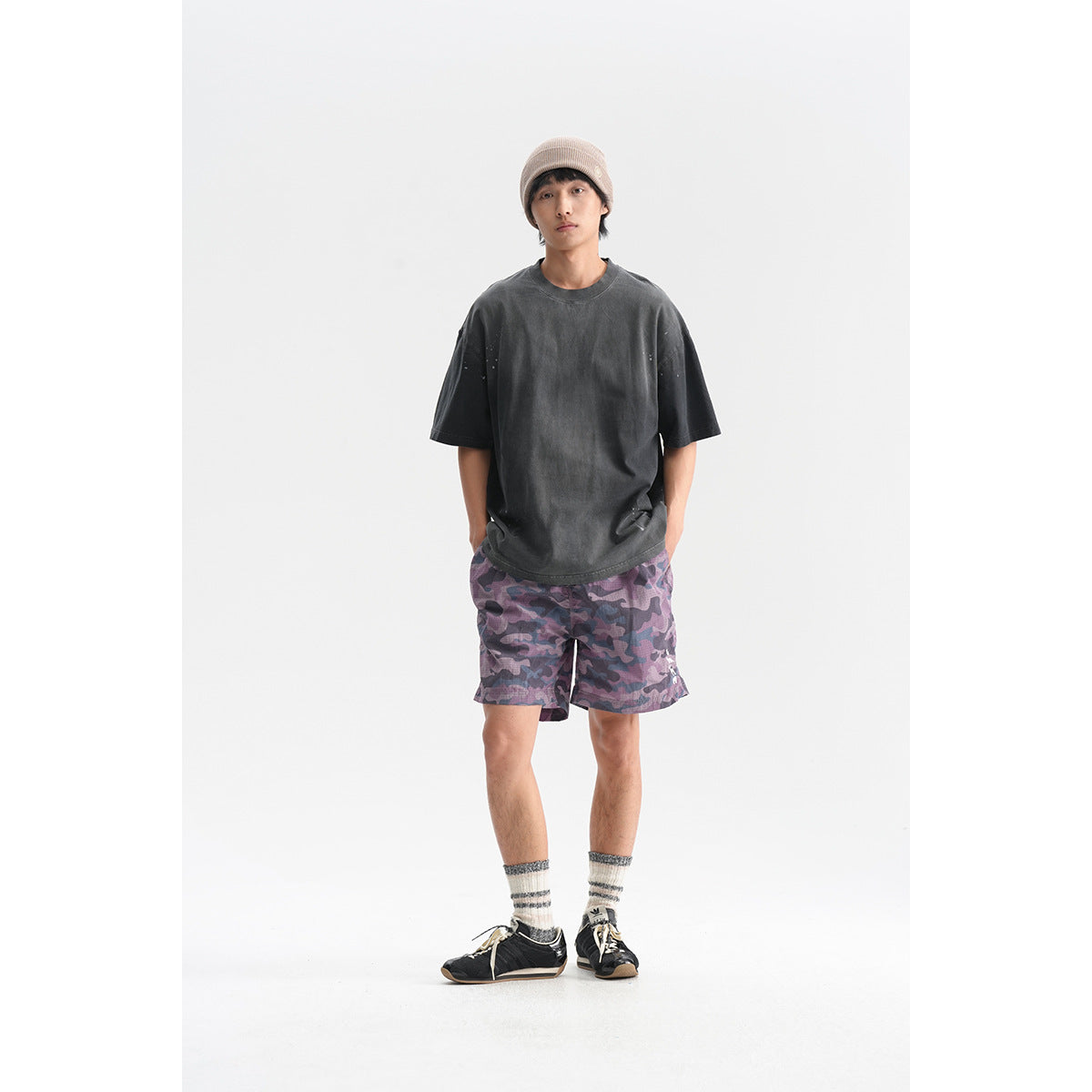 Front view of a model wearing a charcoal oversized T-shirt, purple camouflage shorts, and a beige knit beanie.