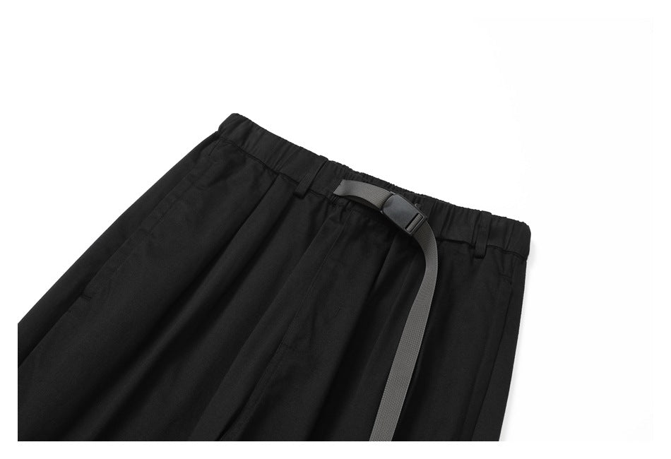 Black trousers laid flat against a white background, with an elastic waistband and long dark webbing belt.