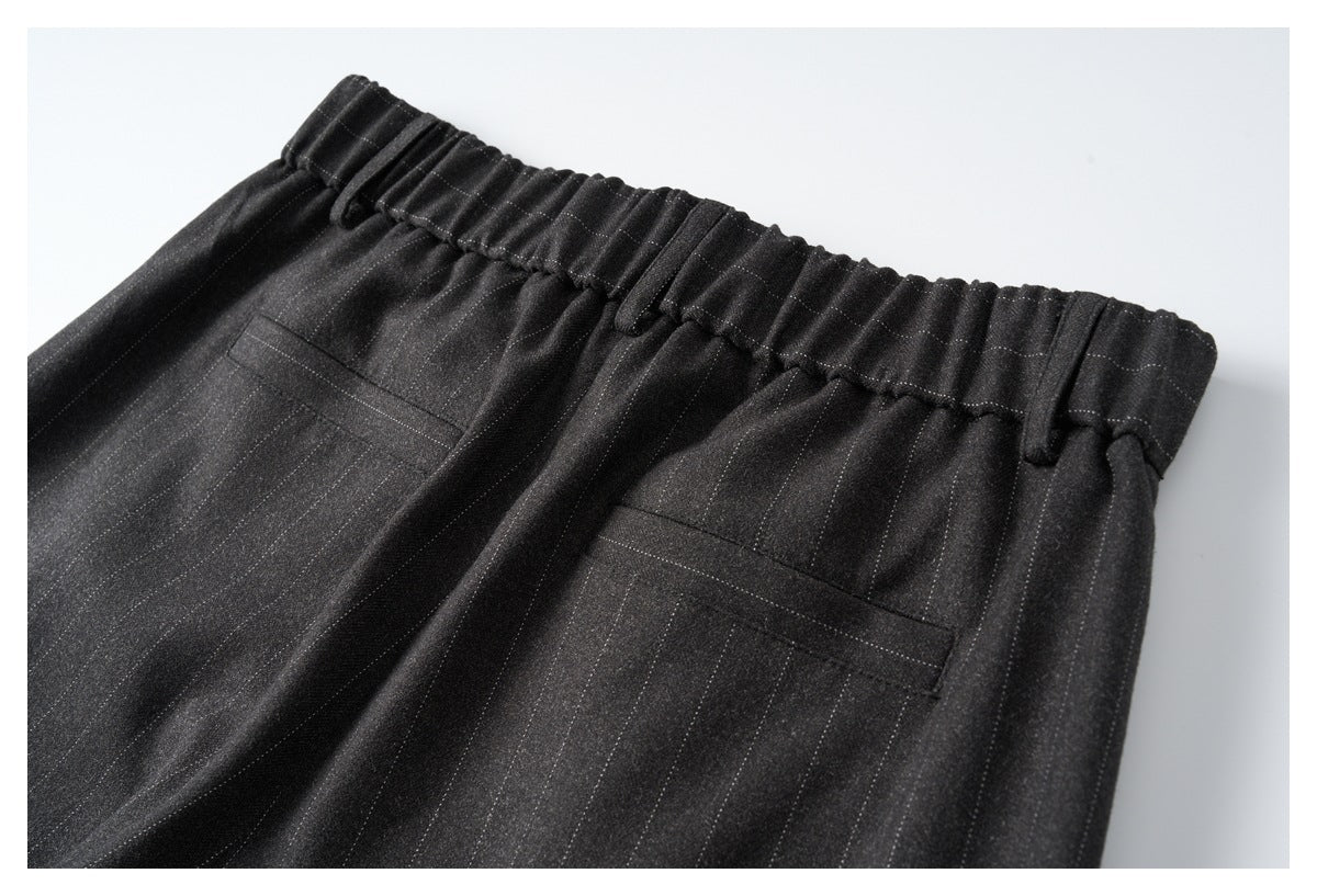 Close-up of black pinstripe trousers with an elastic waistband, belt loops, and two welt pockets.