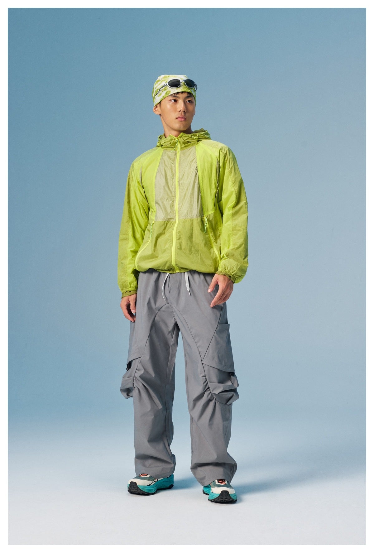 Man wears a lime green color-block hooded jacket with gray cargo pants and a patterned head wrap.
