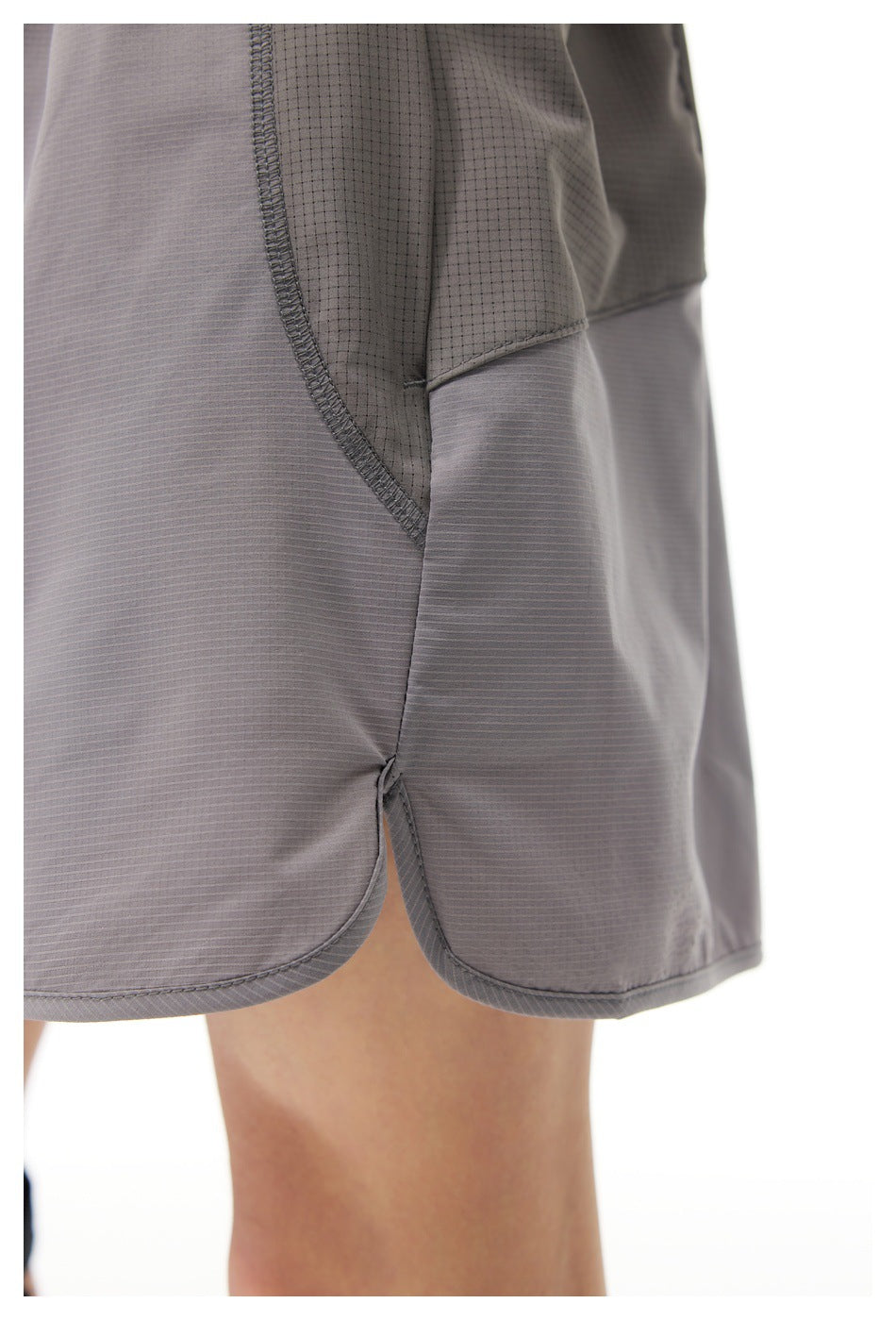 Close-up of gray shorts worn on a person, showing a contrast pocket panel, curved seam, and rounded hem.