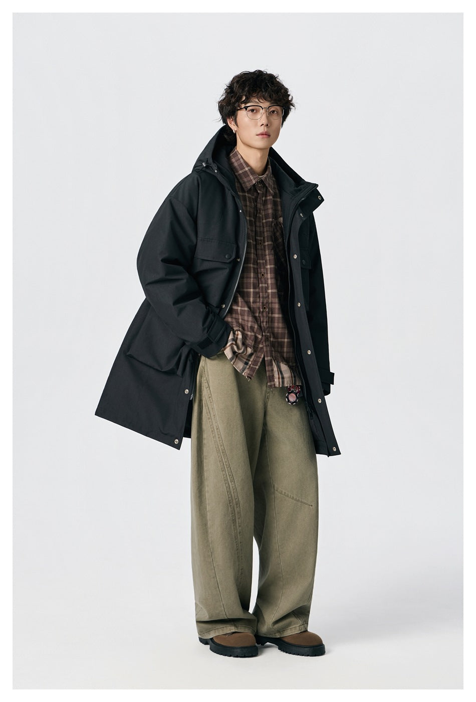 Model in a black hooded parka, shown at an angle with the coat open over a plaid shirt.