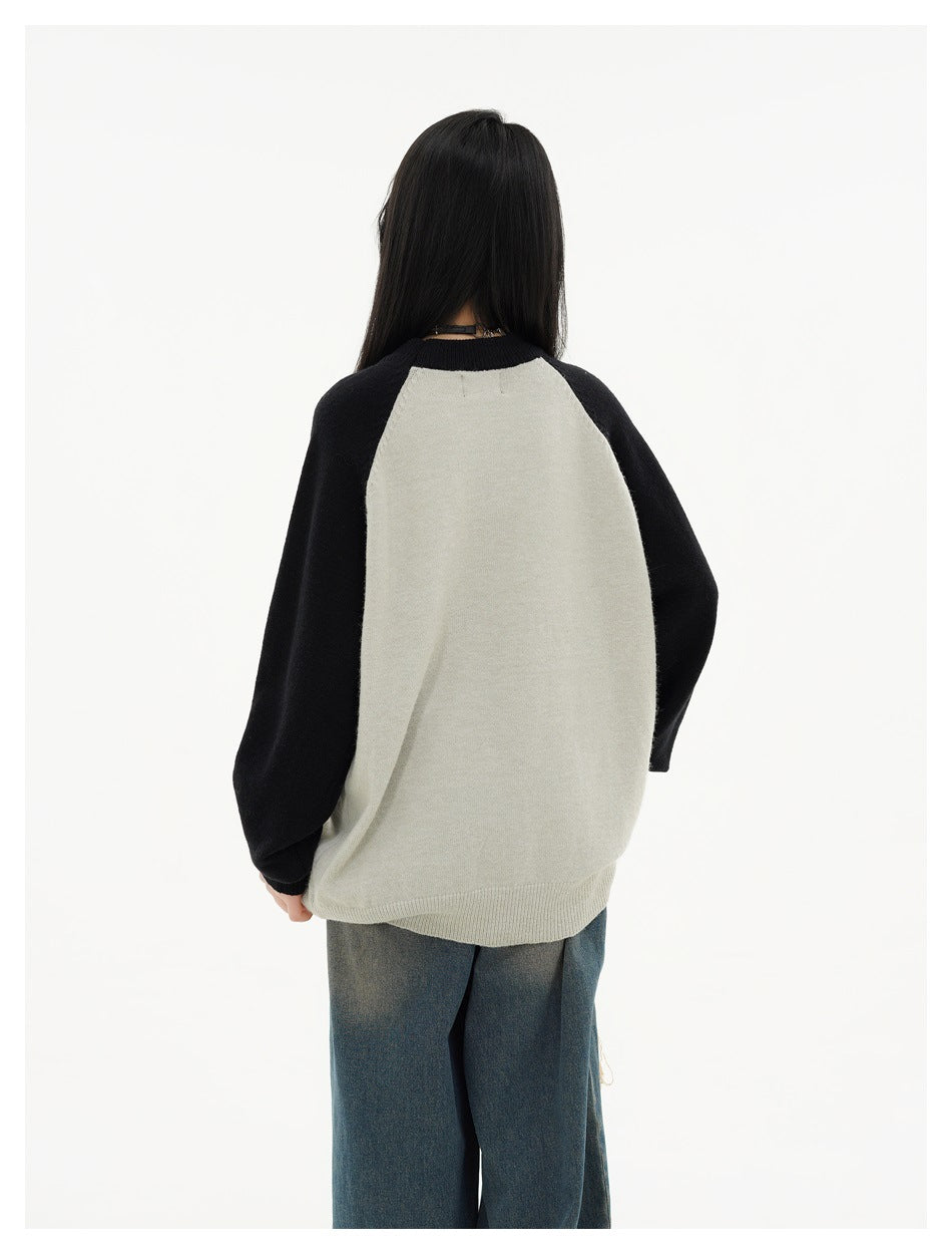 Back view of a model wearing a light gray raglan sweater with black sleeves and blue jeans.
