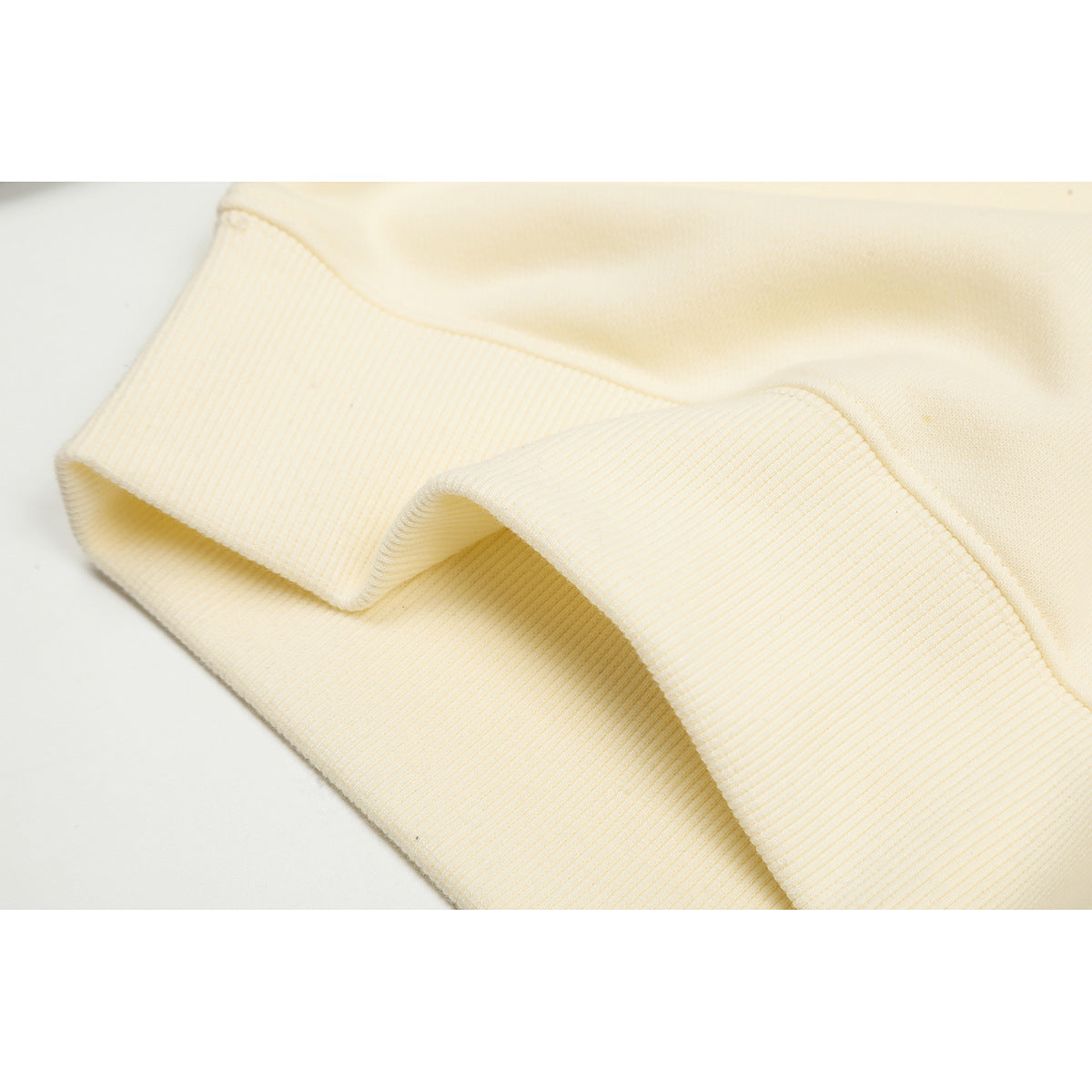 Close-up of a cream sweatshirt's ribbed cuff and folded sleeve.