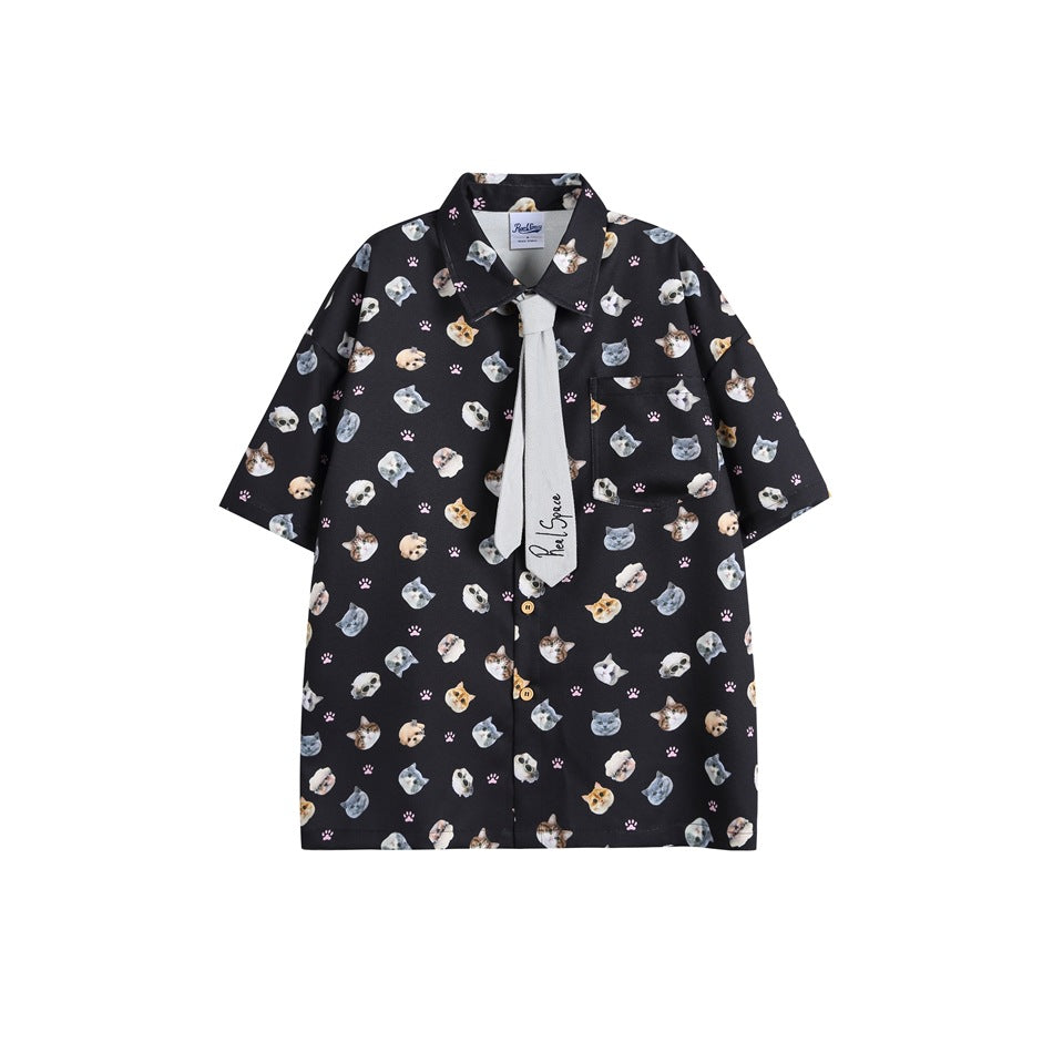 Black short-sleeve shirt with all-over cat face and paw print, chest pocket and gray tie, flat front view