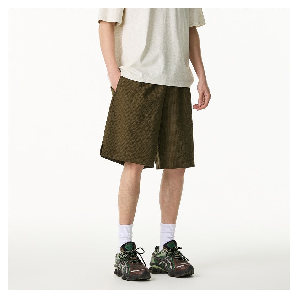 Front three-quarter view of a model wearing olive textured knee-length shorts with a light T-shirt and sneakers.